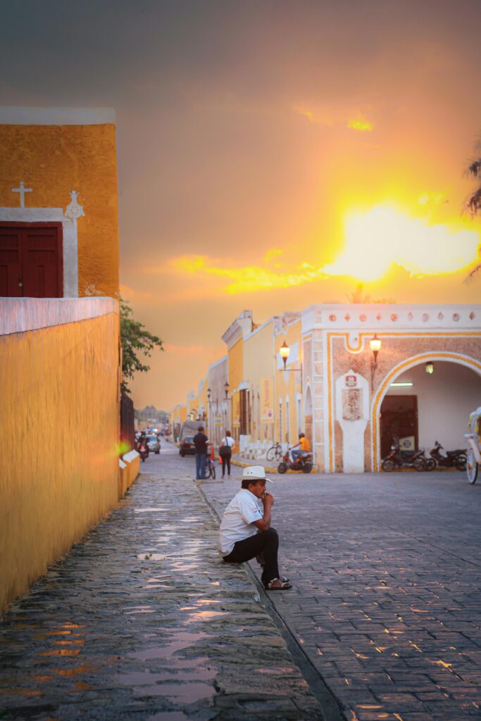 A serene scene in Izamal at sunset with a man sitting on cobblestone streets admiring the golden glow.