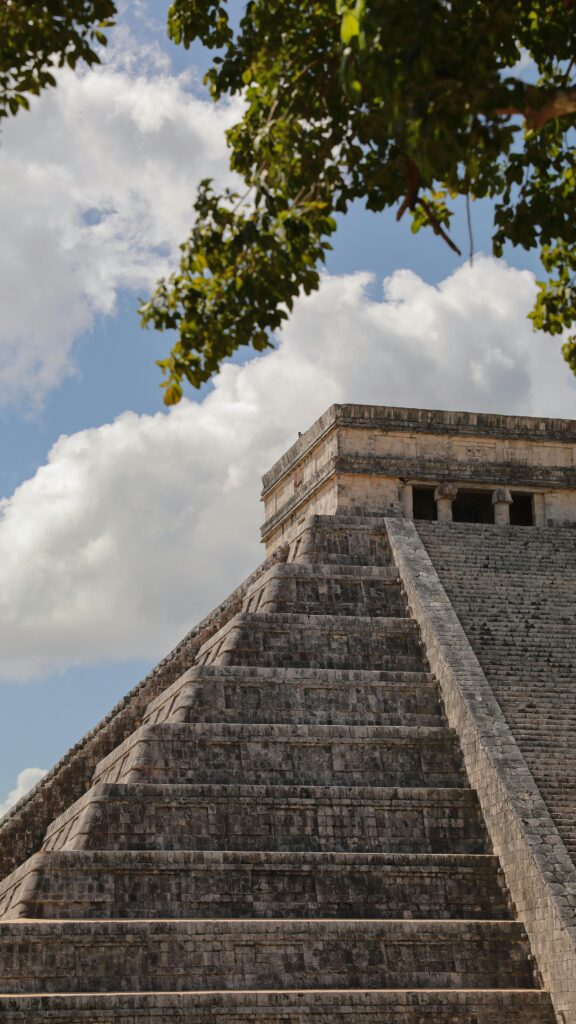 View of the iconic El Castillo pyramid at Chichen Itza under a bright blue sky with clouds.